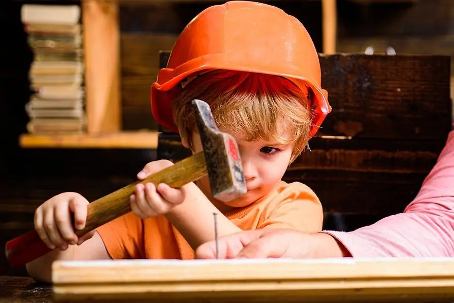Ett barn med orange skyddshjälm siktar på en spik med en hammare.