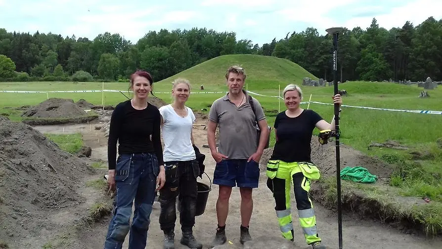 Arkeologerna Alexandra Sanmark, Marta Lindeberg, Mathias Bäck och Kristina Jonsson stå i ett uppgrävt område med Anundshög i bakgrunden.