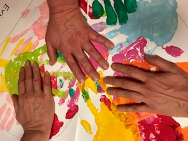 Händer med färg gör handavtryck på ett papper. 