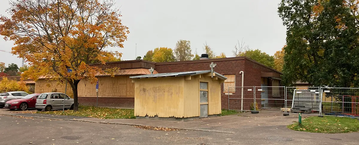 Fotografi på ett hus med gul panel som är i dåligt skick. Bakom står ett brunt tegelhus där fönstren är igenbommade med byggskivor.