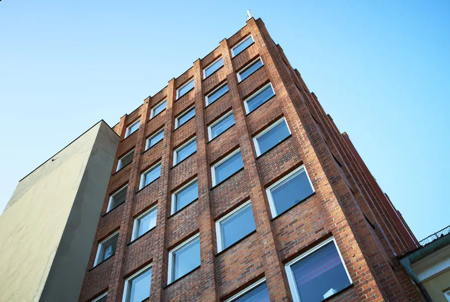 Perspektivbild upp mot tegelröd fasad med rader av fönster som möter den ljust putsade byggnadskroppen. Foto: Lasse Fredriksson