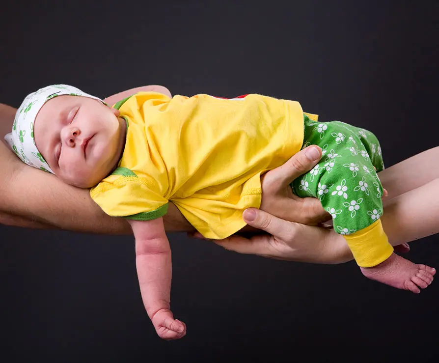På bilden ser två armar som håller i en baby.