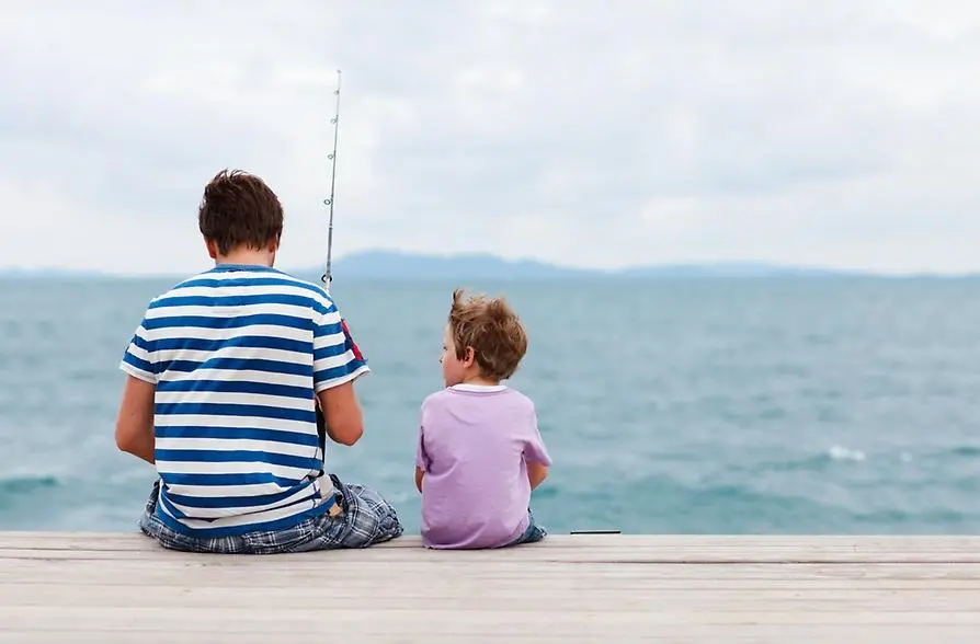 En man och en pojke med fiskespö på en brygga vid vattnet.