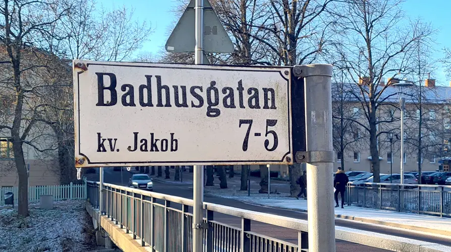 Skylt på stolpe med gatan och kvarterets namn med texten Badhusgatan 7-5 kv. Jakob.