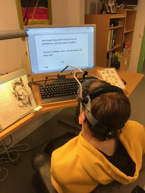 Person med hjälpmedel sitter vid en dator och skriver. 