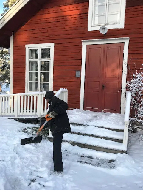 Person skottar framför ett hus på Vallby friluftsmuseum. 