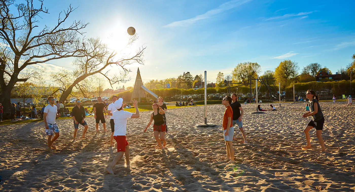 Glada ungdomar spelar volleyboll i solnedgången en varm sommarkväll. 